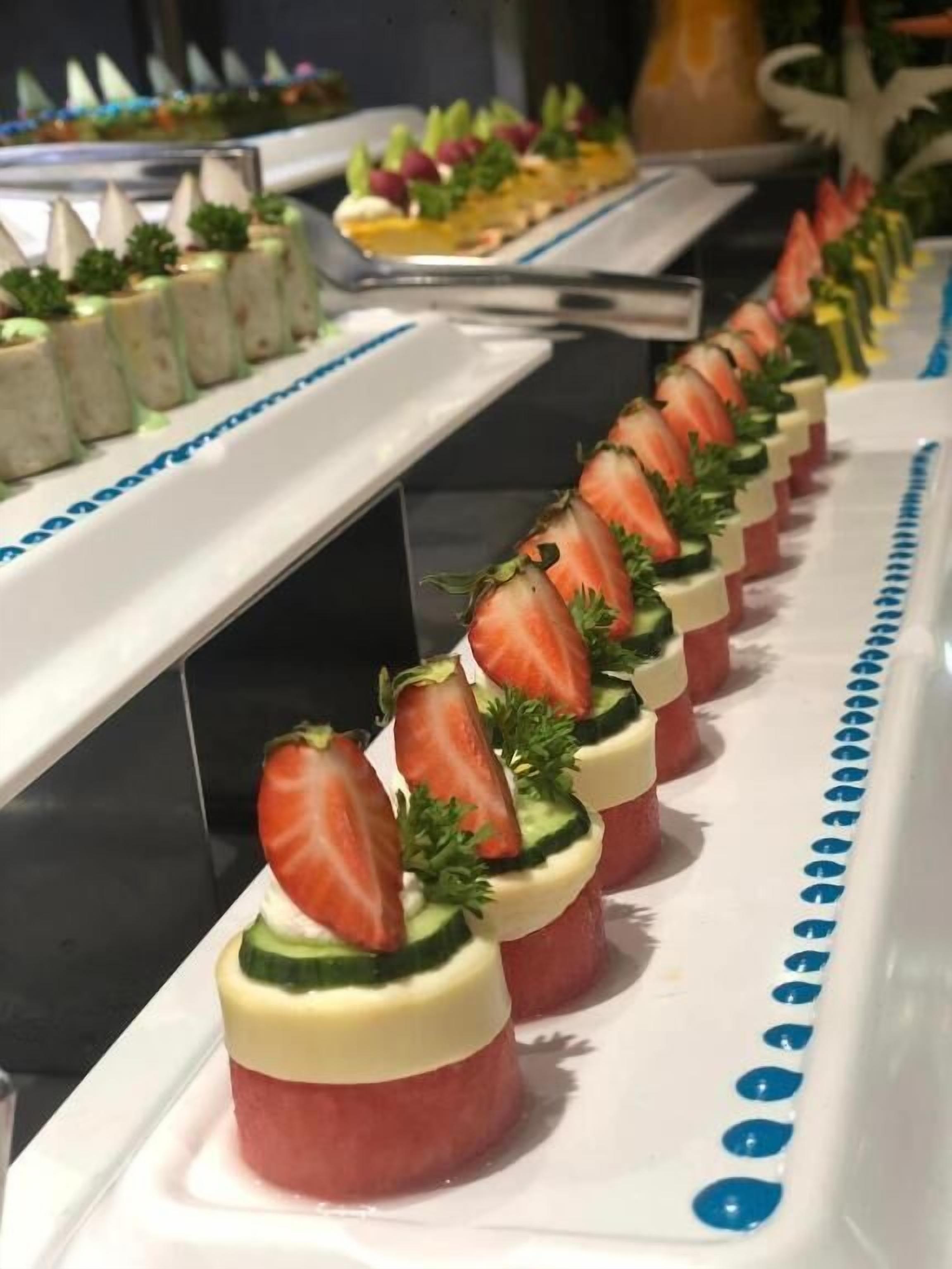 A buffet table with various food items, including a row of strawberry-topped desserts.
