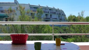 Een balkon met een tafel, rode en groene bekers, en uitzicht op een meerhoog gebouw met balkons.
