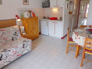 Un espace de vie compact comprenant un coin cuisine, un coin repas et un canapé recouvert d’un tissu imprimé de motifs de journaux.