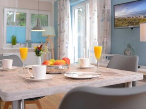 A dining area with a wooden table, two white cups, two glasses of orange juice, a bowl of fruit, and a clock on the wall. - Florida app. 3 Wednesday (Ostseebad Boltenhagen)