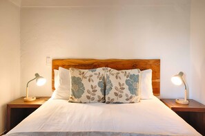 A neatly made bed with floral pillows, a wooden headboard, and two bedside lamps on wooden nightstands.
