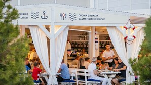 Restaurante al aire libre con toldos blancos y mesas, con temática náutica que incluye anclas y motivos de olas.