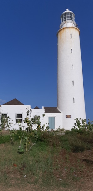 Een hoge witte vuurtoren met een klein bijgebouw, voorzien van een groene deur en ramen.