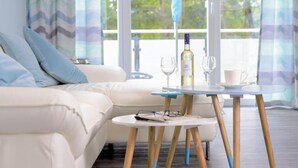 Een moderne woonkamer met een bank, een klein rond tafeltje met een fles en glazen, en uitzicht op groen.