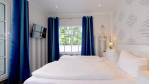 Een hotelkamer met een groot bed, een televisietoestel, een raam met gordijnen, en een wand met decoratie in nautisch thema.