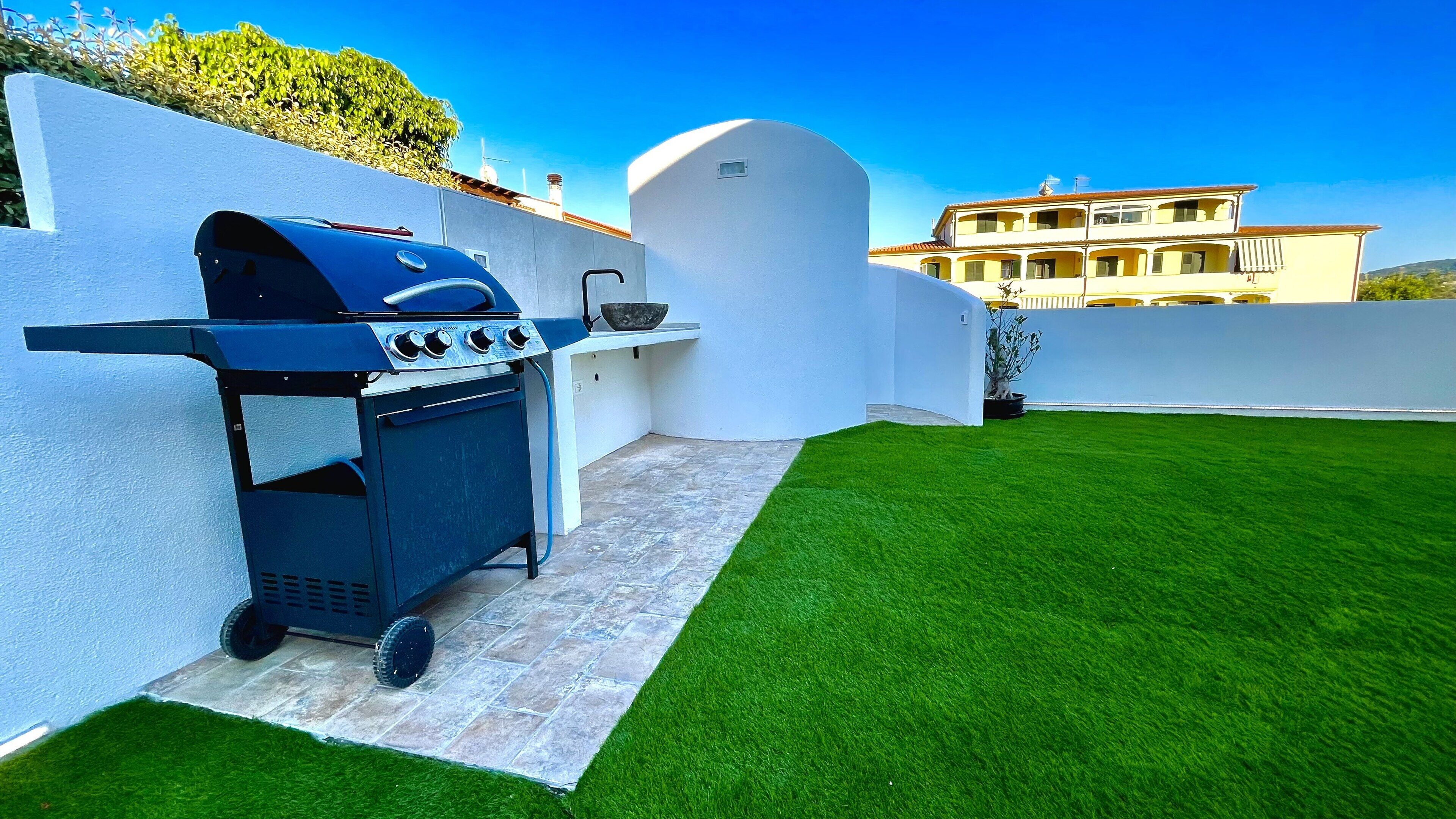 Eine Terrasse mit einem Grill, einer weißen Wand und einem Gebäude im Hintergrund.