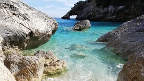 Paesaggio costiero roccioso con acque turchesi cristalline e una formazione rocciosa imponente.