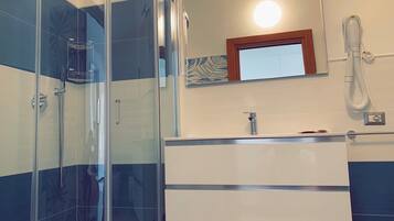 A modern bathroom with a glass-enclosed shower, a white vanity with a mirror, and a handheld showerhead.