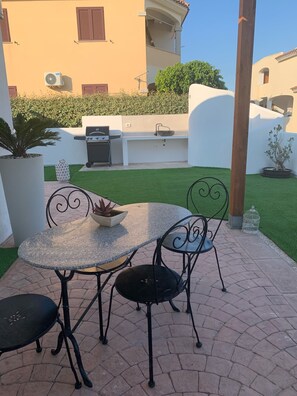 An outdoor patio with a round table and two chairs, a grill, and a small garden area with a potted plant. - The residences of the sea 4 (La Caletta)