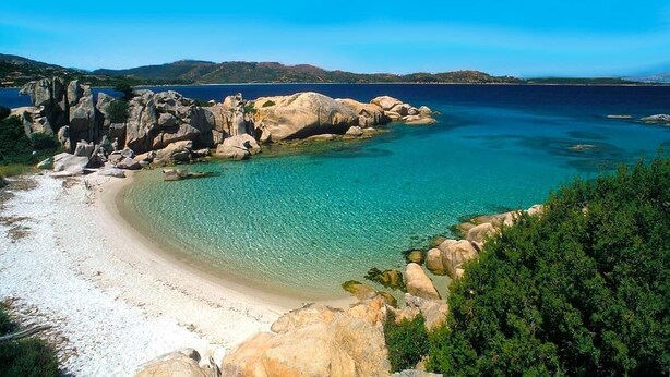 Paesaggio costiero con acque cristalline turchesi, spiaggia di sabbia bianca e grandi massi.