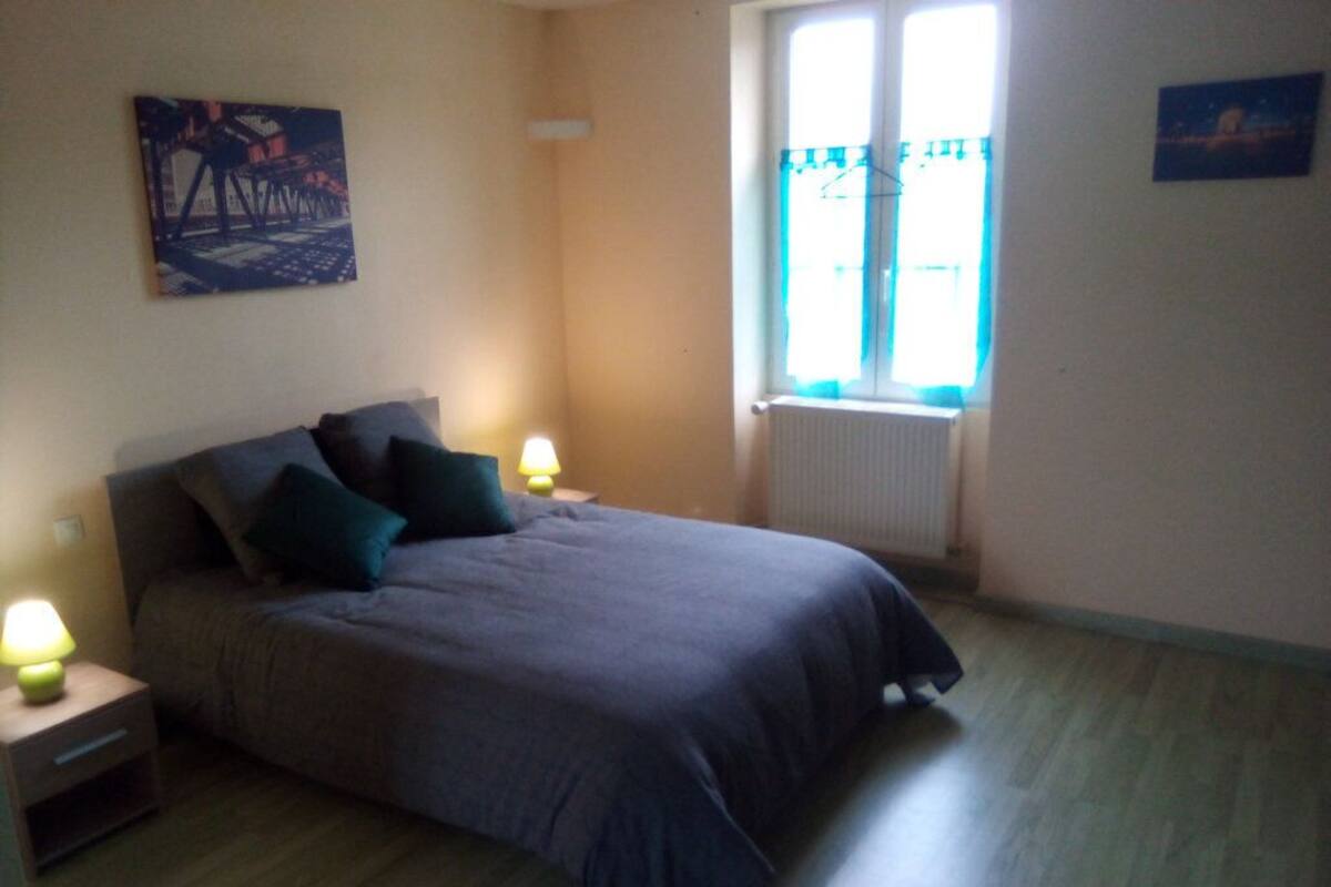 A bedroom with a bed, two bedside lamps, a radiator, and a window with curtains.