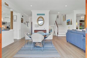 A modern living room with a blue sofa, a dining area with wicker chairs and a glass table, and a staircase leading to another level.