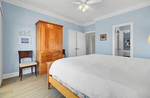 A bedroom with a large bed, wooden wardrobe, a chair, and a ceiling fan.