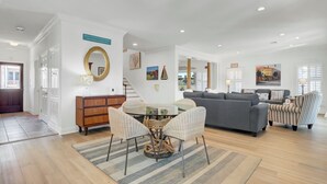 A spacious living room with a grey sofa, striped armchairs, a glass coffee table, and a dining area with wicker chairs.