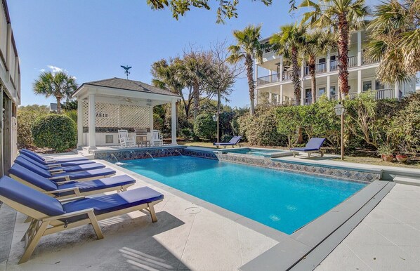 A swimming pool with lounge chairs, a covered seating area, and palm trees.