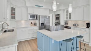A modern kitchen with white cabinetry, stainless steel appliances, a central island, and bar stools.