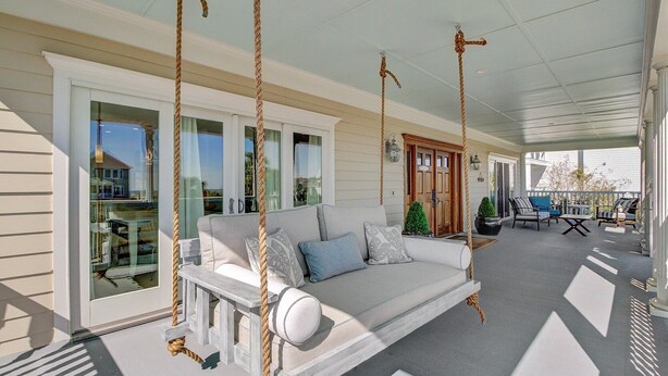 A covered porch with a swing chair, a white sofa with cushions, and a small table.