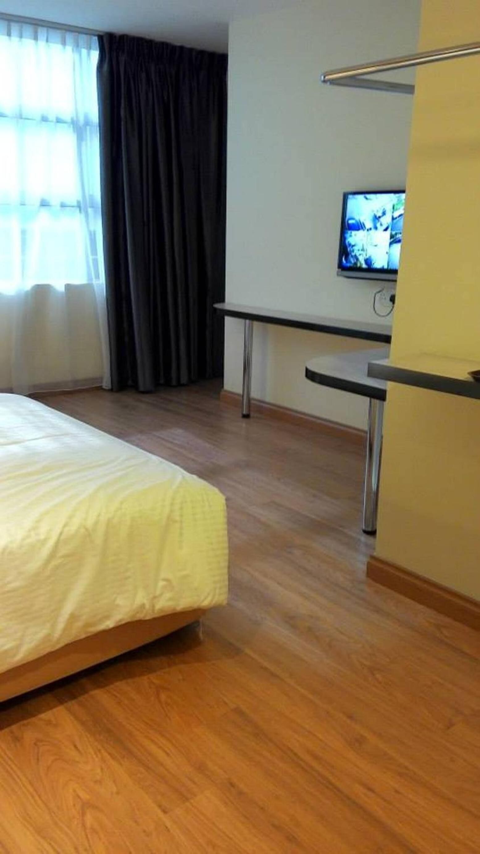 A hotel room with a bed, a desk, a television, and a window with curtains.