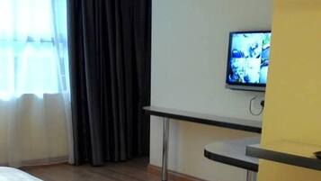 A hotel room with a bed, a desk, a television, and a window with curtains.