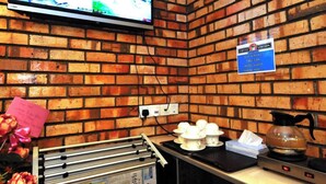 Ett kök med en tegelvägg, en tv som är monterad ovanför bänkskivan och en skylt som visar var kaffestationen finns.