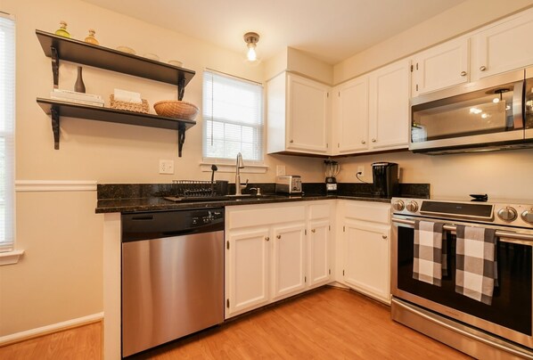 Enjoy cooking in this kitchen with a dishwasher, oven, and microwave, complemented by white cabinetry and a black countertop.