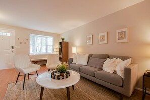 Relax in this inviting living room with a comfortable sofa, armchair, and coffee table, surrounded by framed pictures and a window with shutters.