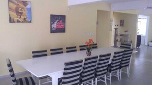 Un comedor con una mesa larga y sillas a rayas, cuadros en la pared y una planta en maceta sobre la mesa.