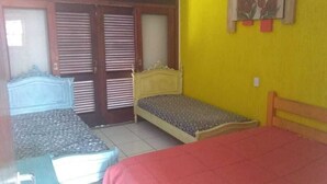 Una habitación pequeña con una cama, un banco y una puerta con contraventanas.