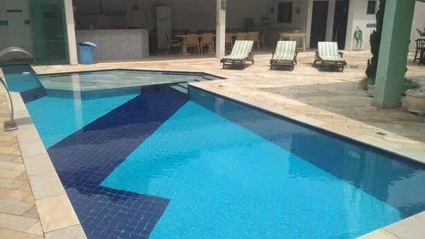 Una piscina con bordes de azulejos, sillas de descanso y un patio con mesas y sillas.