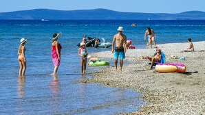 A beach with people in swimwear, some standing in shallow water and others sitting on the pebbly shore. - 4 * apartments superior / 2pax studio-l (Zaton)