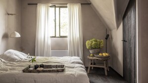 Een slaapkamer met een bed, een raam met gordijnen, een nachtkastje met een potplant en een dienblad met spullen.