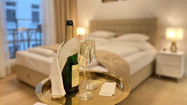 A hotel room with a bed, a bedside table with a lamp, a window with curtains, and a balcony. - Steiner Residences Vorgartenstrasse (Vienna)
