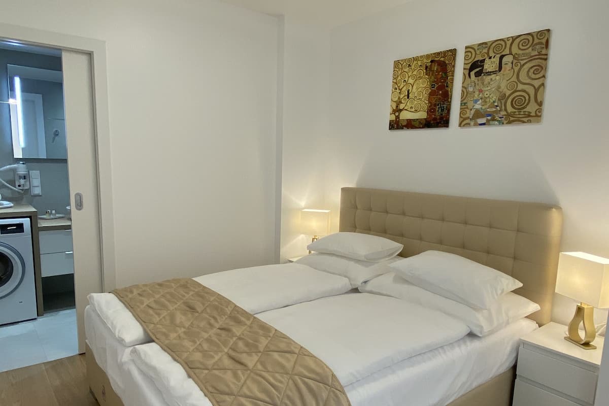 A neatly made bed with a quilted blanket, a bedside lamp, and a nightstand. There are two wall-mounted artworks above the bed.