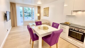 A modern kitchen with white cabinets, a built-in oven, and a dining area with a white table and purple chairs. - Steiner Residences Vorgartenstrasse (Vienna)