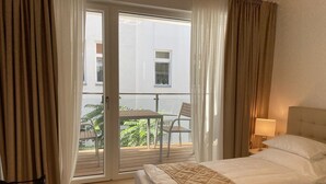 A hotel room with a bed, a small table, and a chair near a sliding glass door leading to an outdoor area with a table and chairs. - Steiner Residences Vorgartenstrasse (Vienna)
