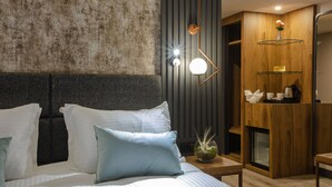 Una habitación de hotel moderna con una cama grande, una mesita de noche de madera, una lámpara de pared y un armario empotrado con estantes.