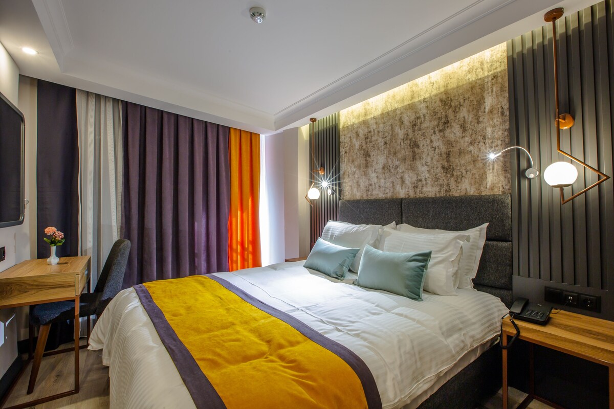 A modern hotel room with a large bed, a desk, and a chair.