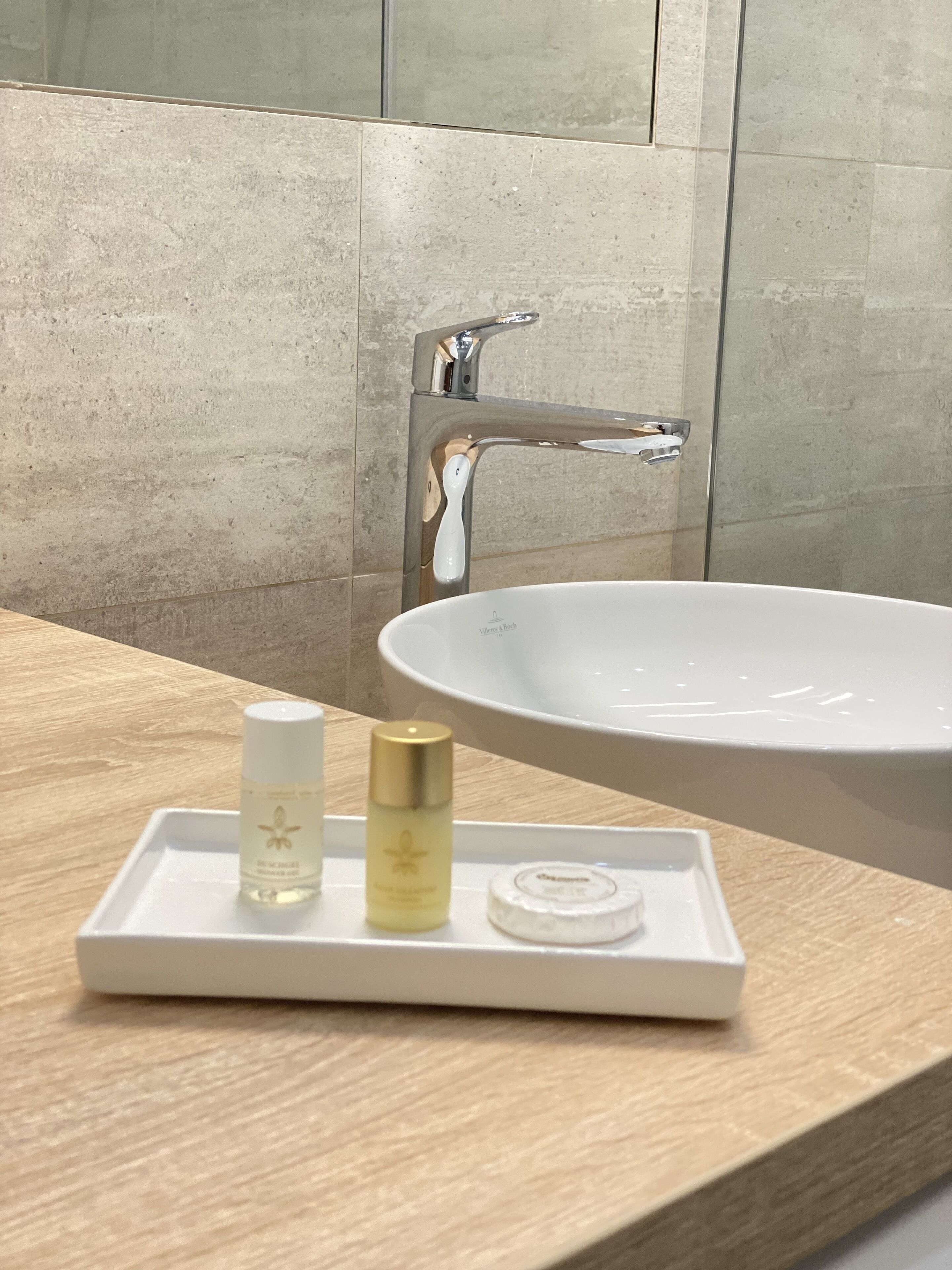 A bathroom with a white sink, a mirror, and a tray with skincare products.