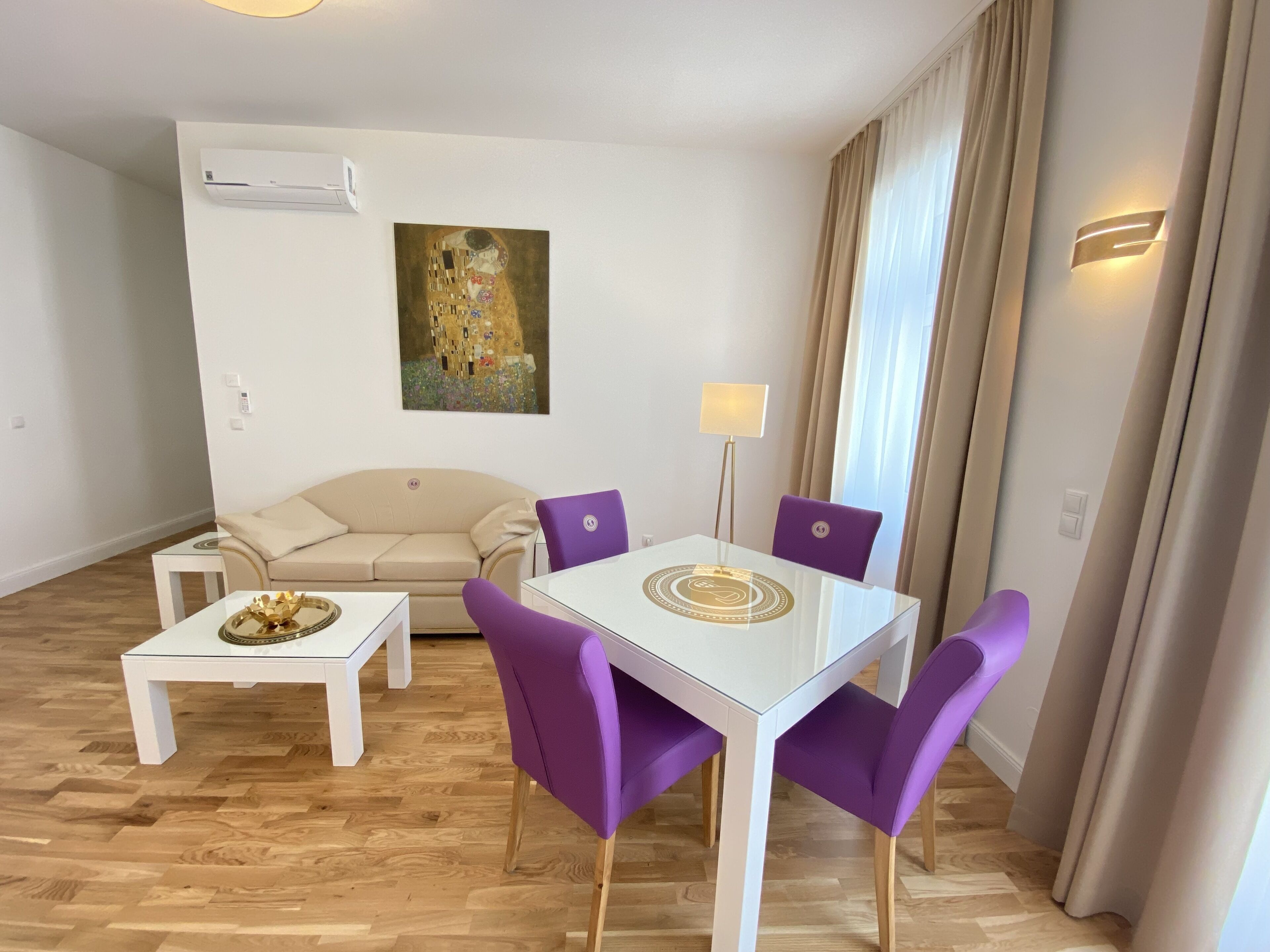 A modern living room with a glass dining table, purple chairs, a beige sofa, and a painting on the wall.