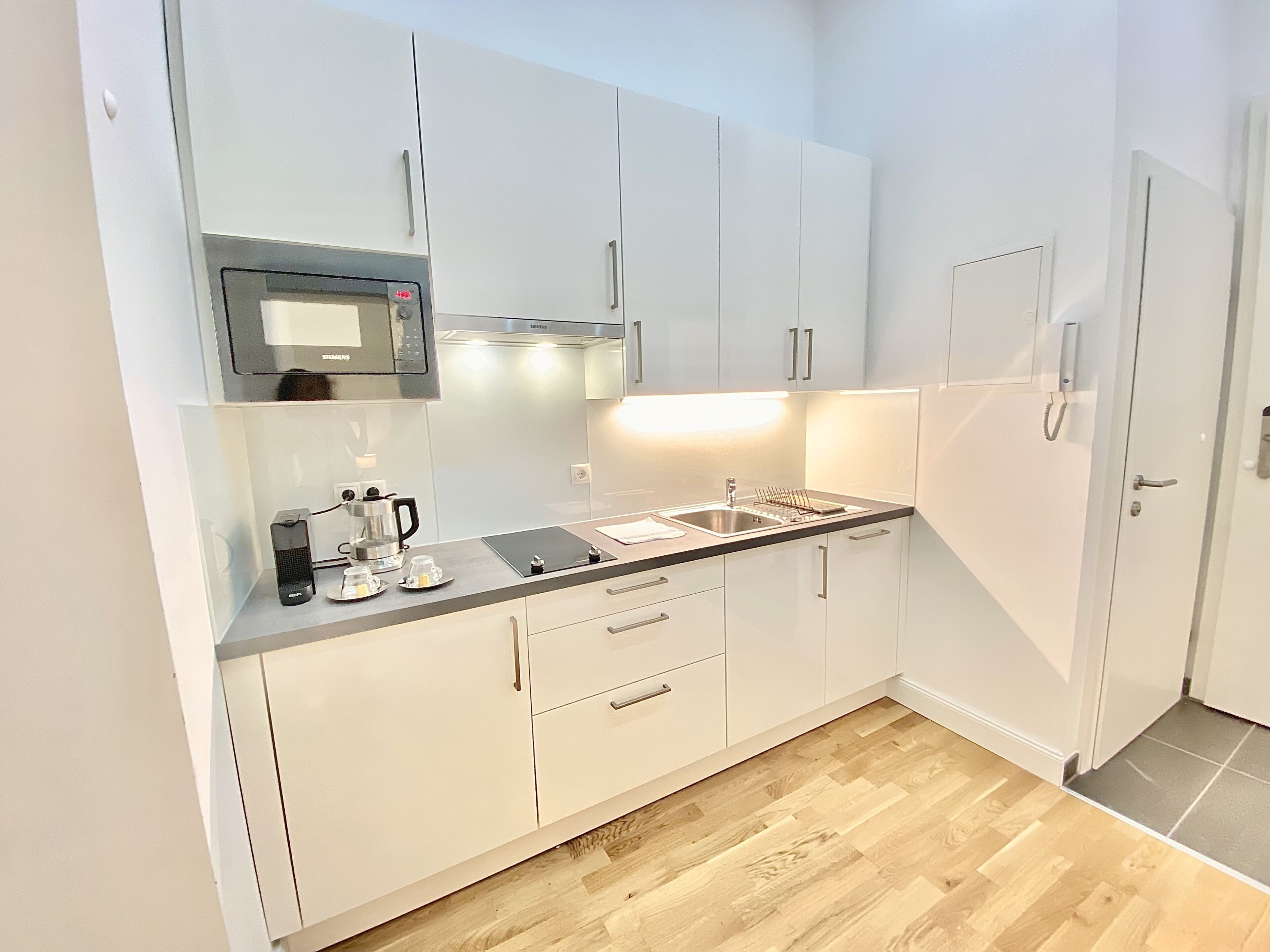 A modern kitchen with white cabinets, a stainless steel sink, a coffee maker, and a microwave.
