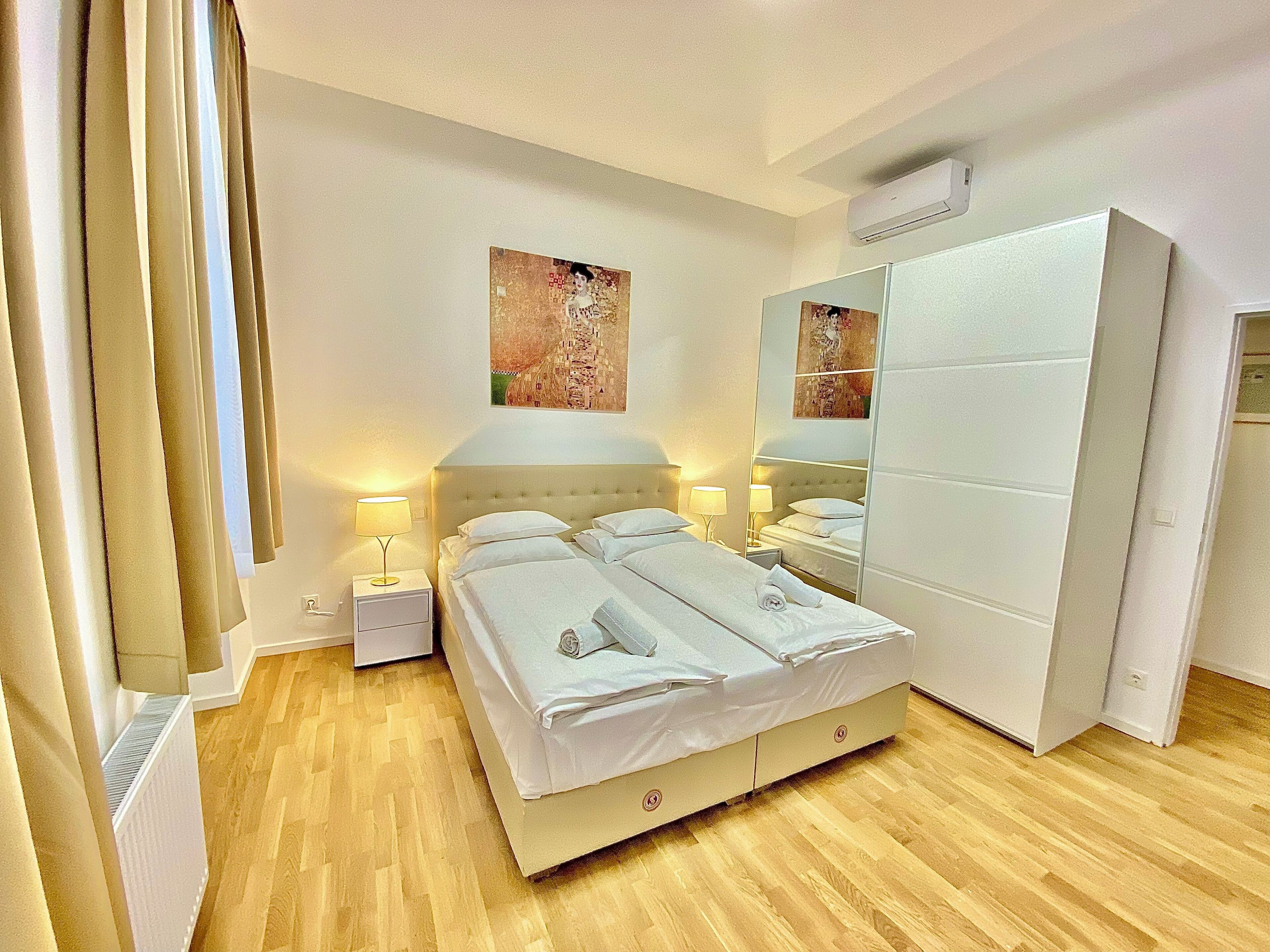 A hotel room with a bed, bedside tables, a wardrobe, and artwork on the walls.