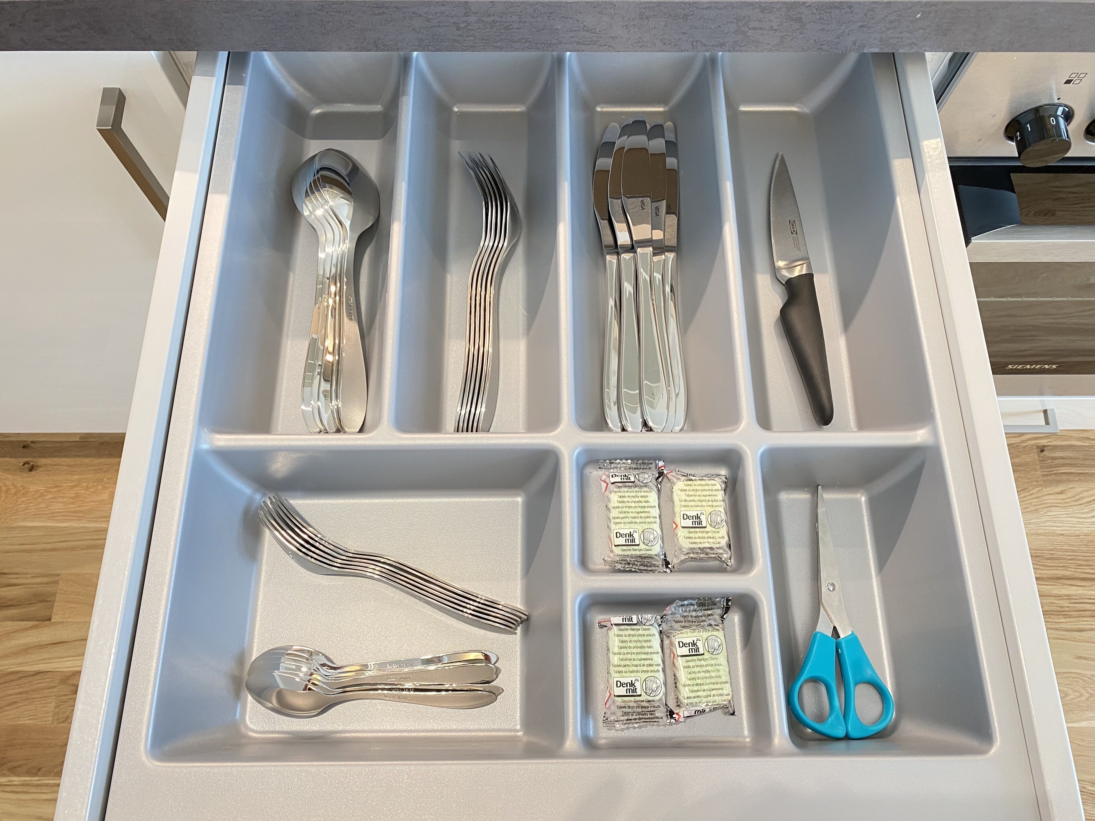A drawer with compartments containing various kitchen utensils and packaged items.