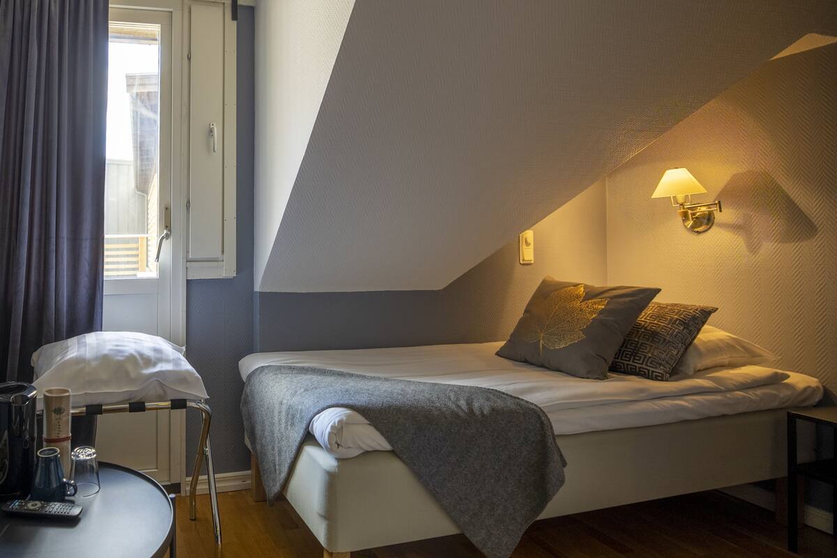 Une chambre à coucher de taille modeste, comprenant un lit simple, une table de chevet avec une lampe et une fenêtre avec des rideaux.