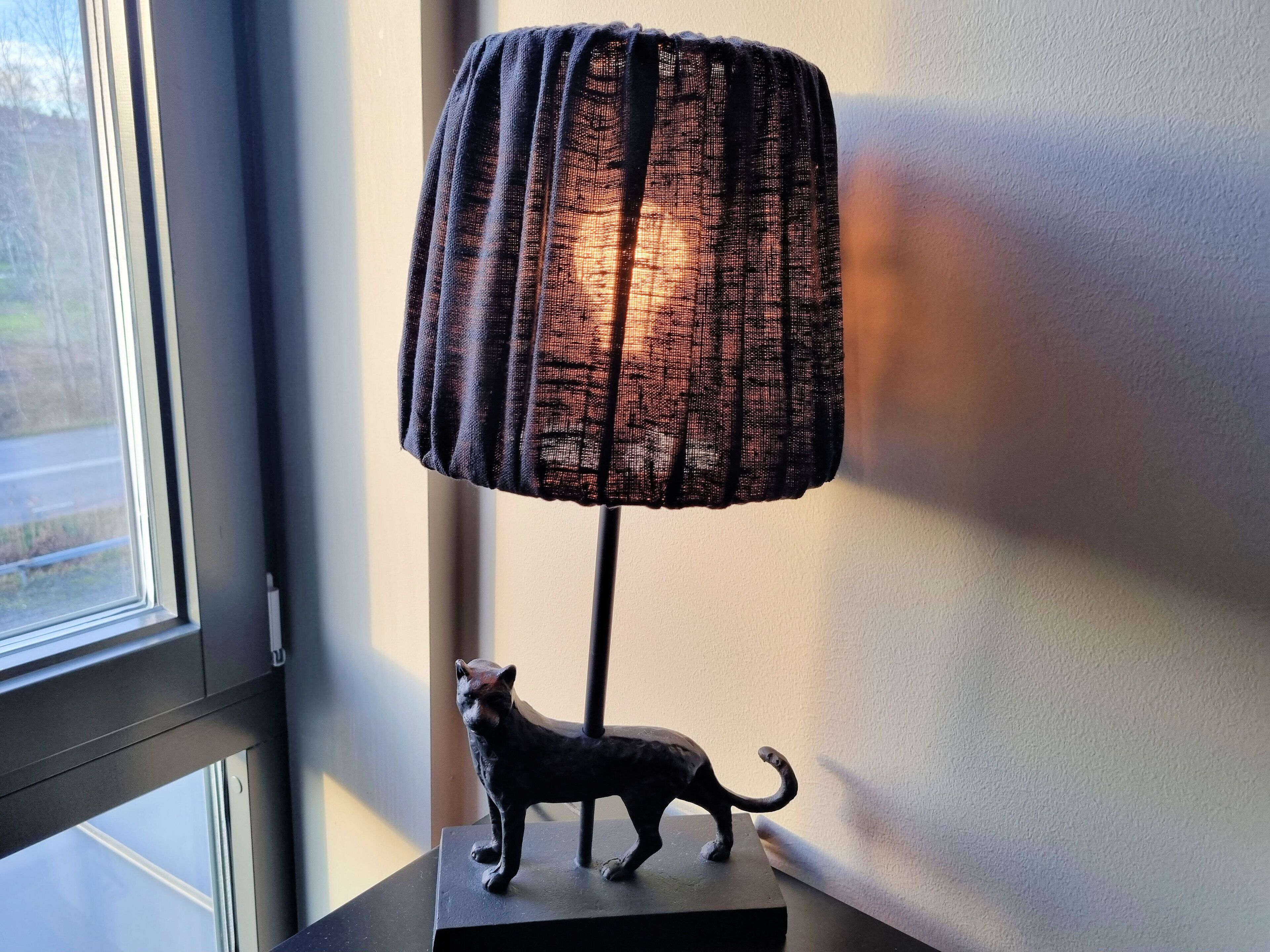 En lampe med en struktureret skærm og en lille dyrefigur på et stativ.