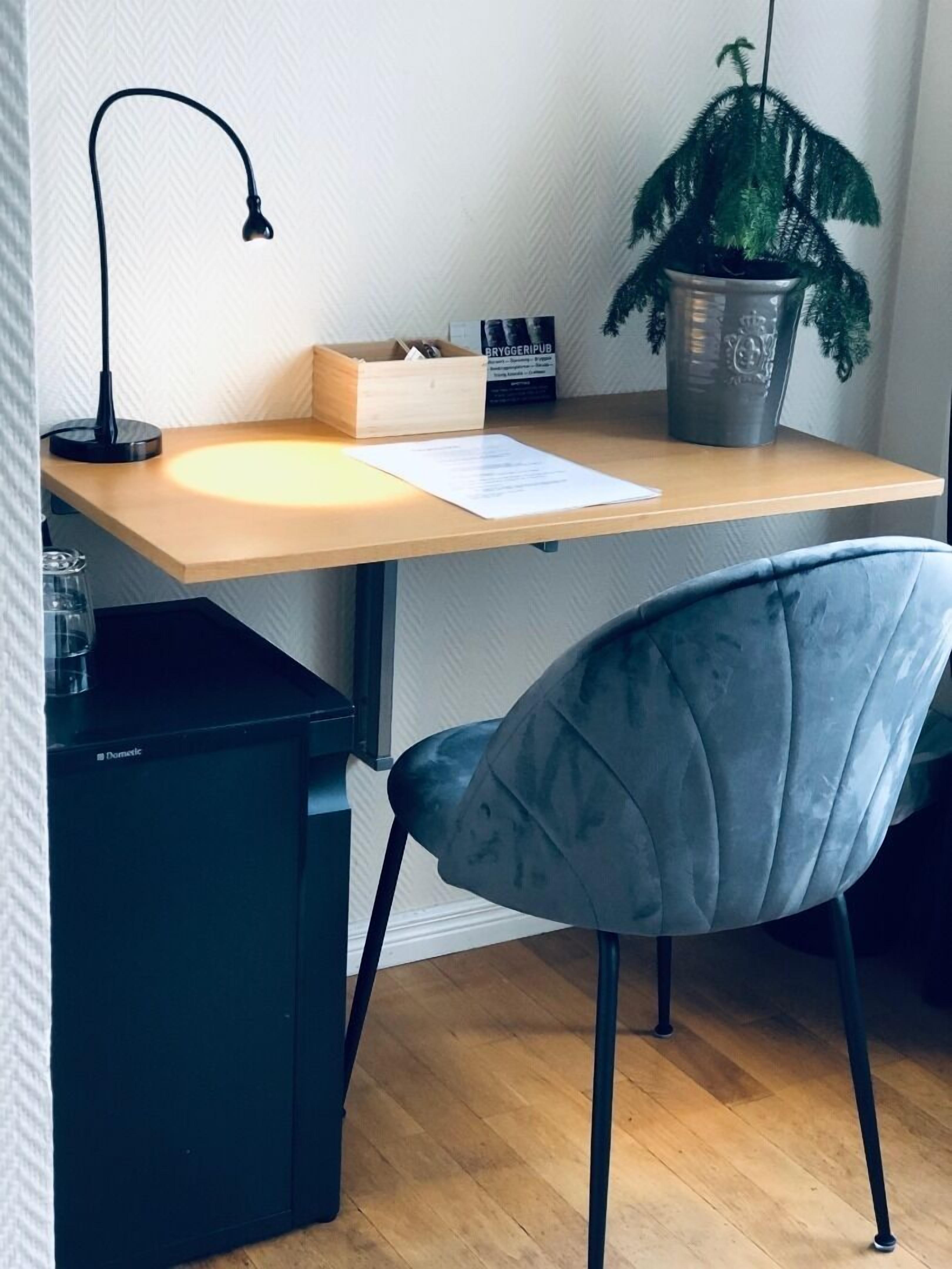 A workspace with a wooden desk, a black lamp, a grey chair, a potted plant, and a Dometic coffee machine.