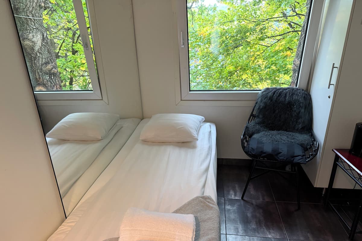 Une chambre avec deux lits, une chaise et une fenêtre donnant sur des arbres.