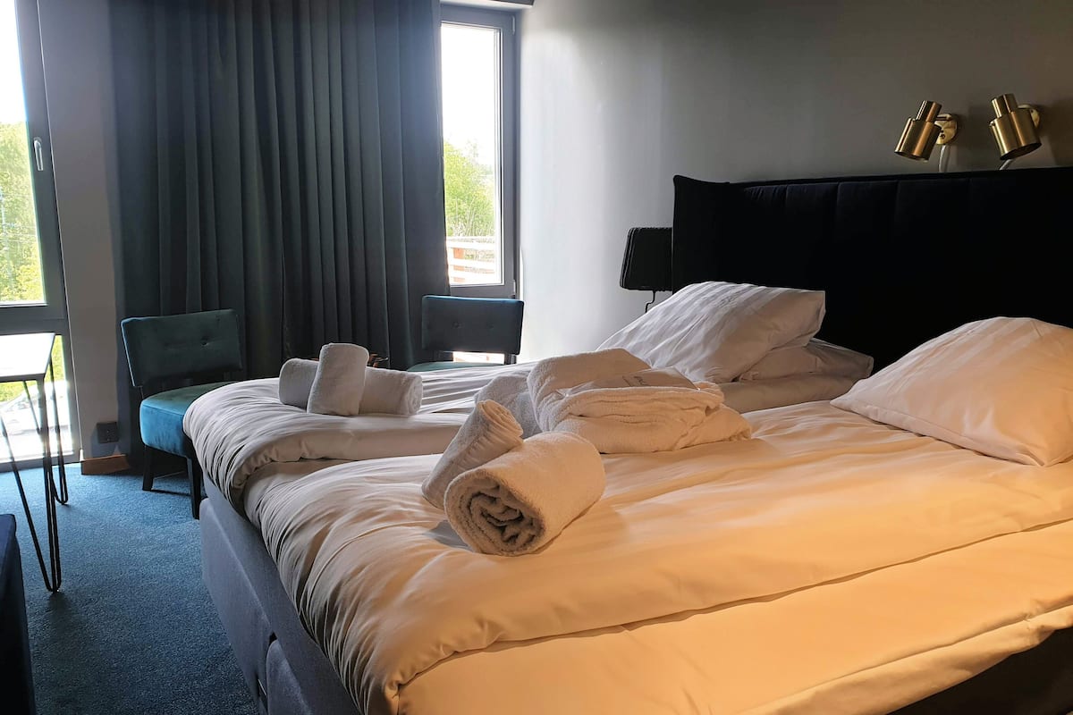 Une chambre d’hôtel avec un lit bien fait, une chaise, un bureau et une fenêtre avec des rideaux.
