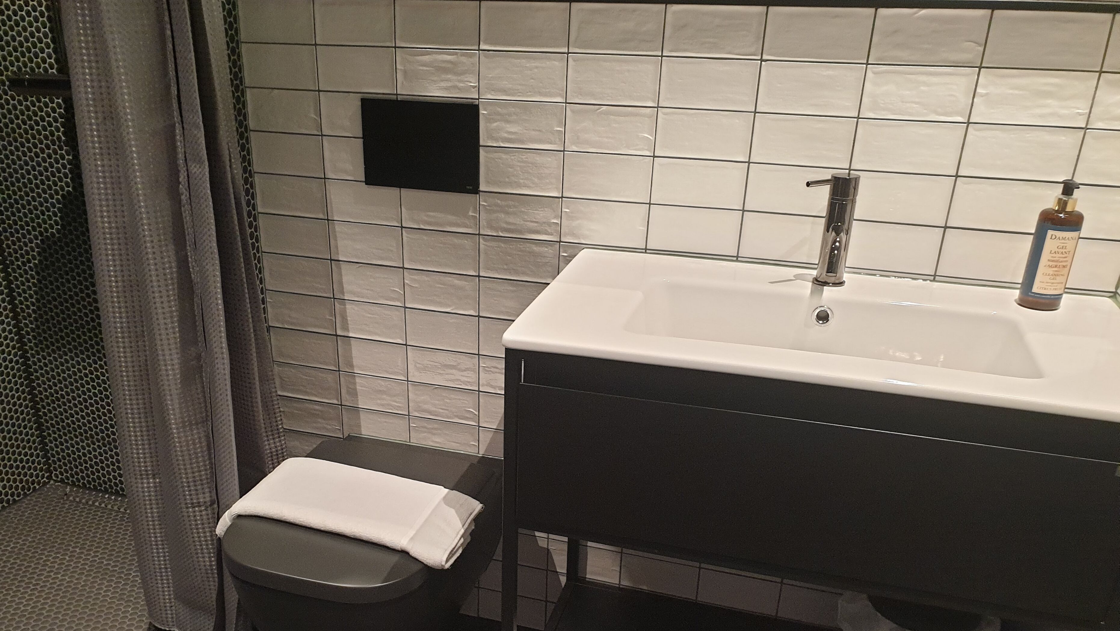 Ein Badezimmer mit Waschbecken, schwarzem Schrank und einer kleinen Bank mit weißem Handtuch.