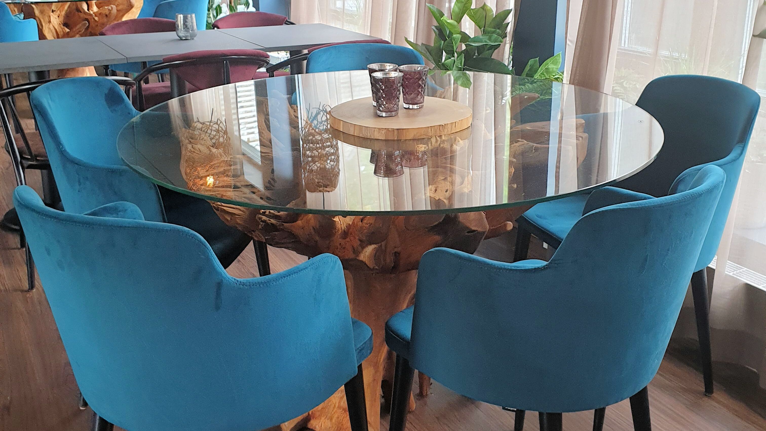 Une table ronde en verre, dotée d’un pied en bois, est entourée de chaises bleues.