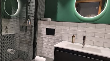 Un baño moderno con cabina de ducha de vidrio, un lavamanos blanco sobre encimera negra y un espejo con marco circular.
